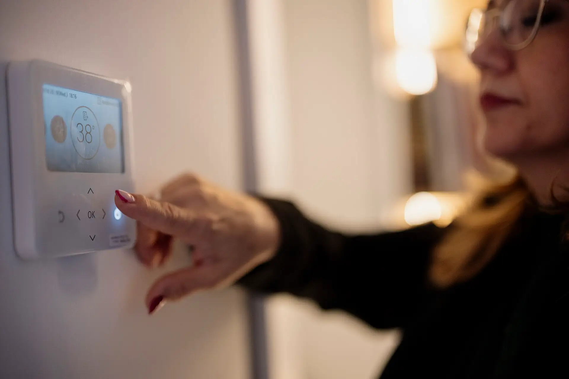 A hand adjusting a wall-mounted digital thermostat