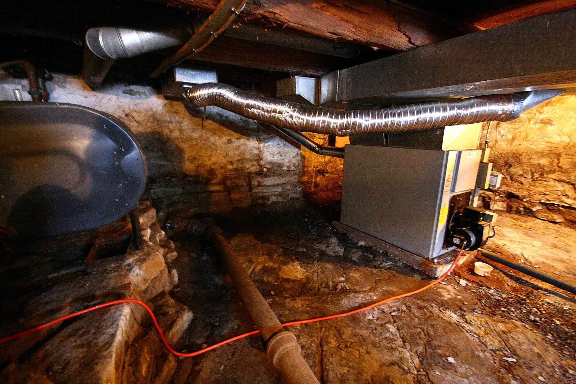 An unfinished basement with a furnace and metal ductwork