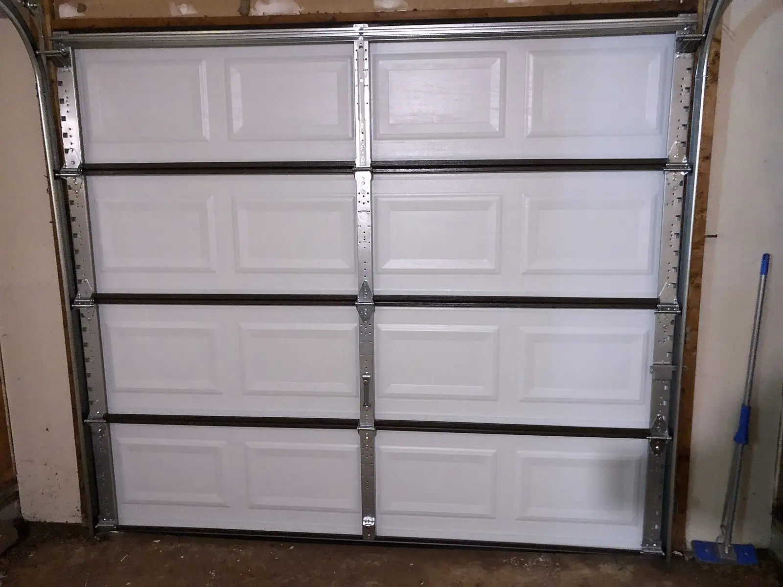 The inside of a white steel single-car garage door with its tracks and hinges
