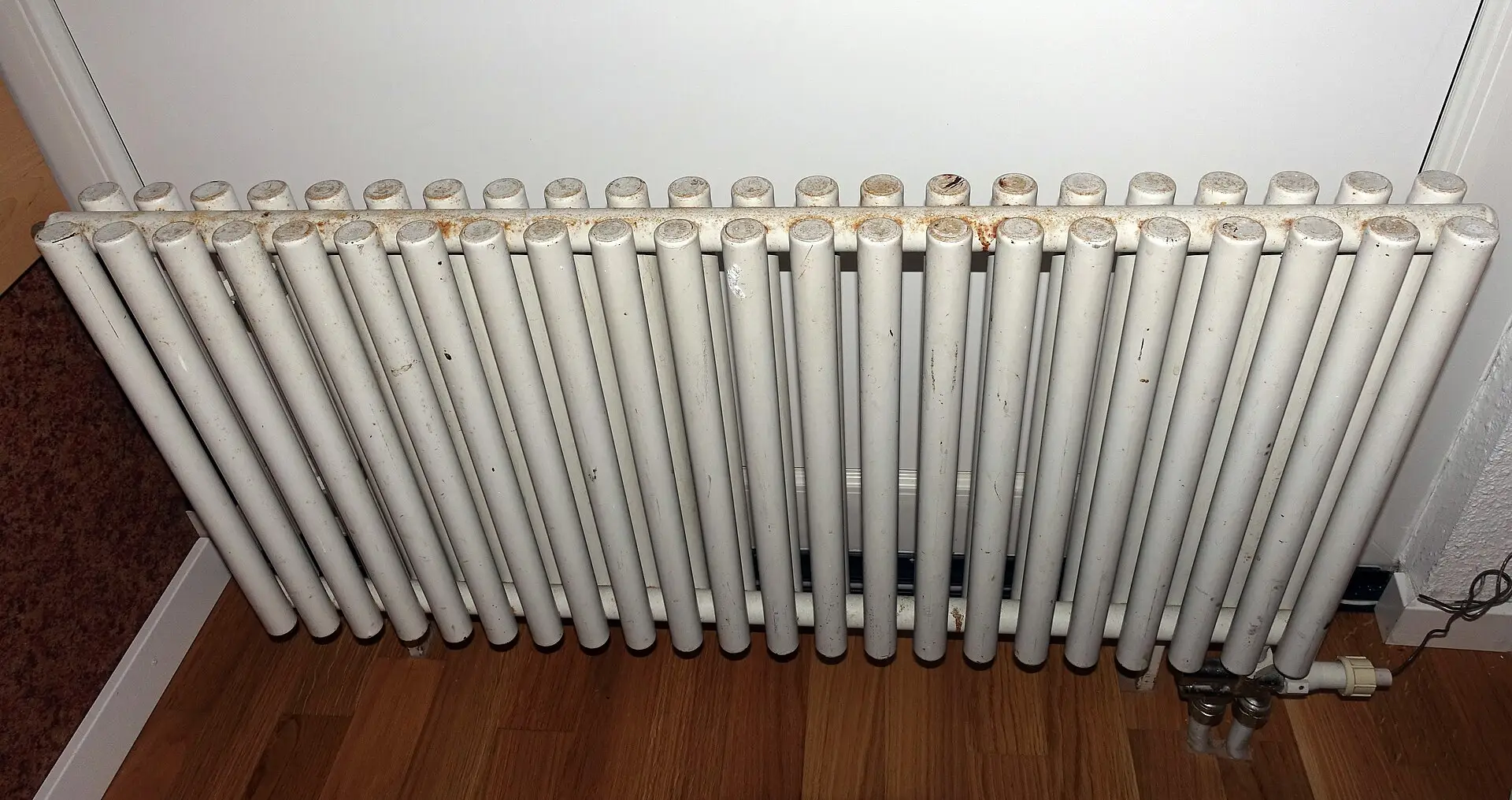 A white column radiator against a wall above a wood floor