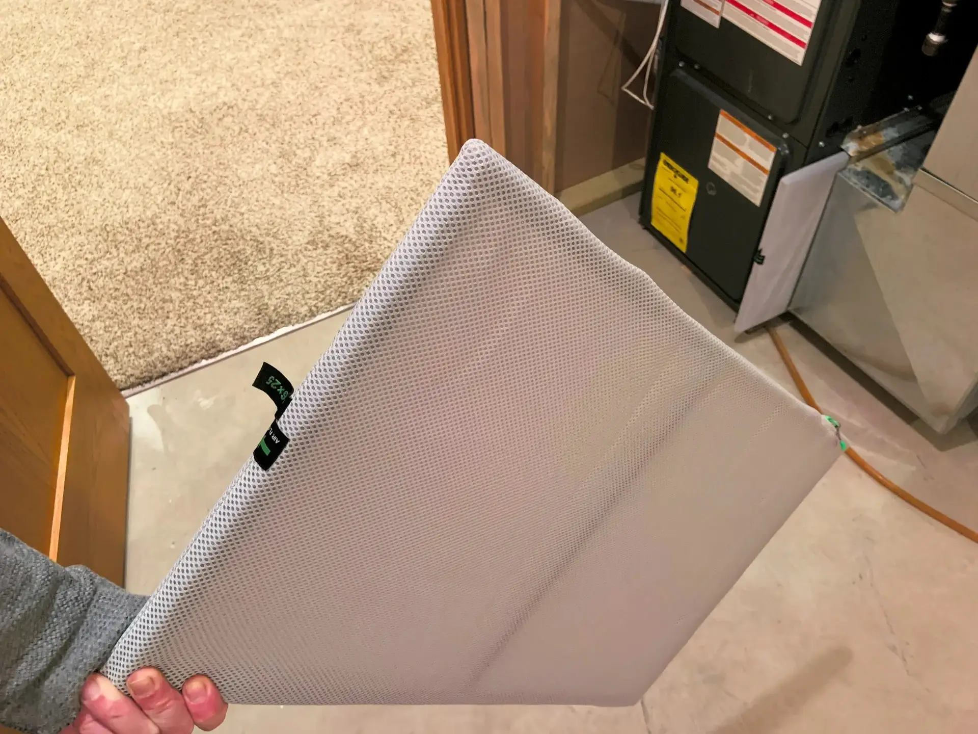 A pleated HVAC air filter held next to a furnace