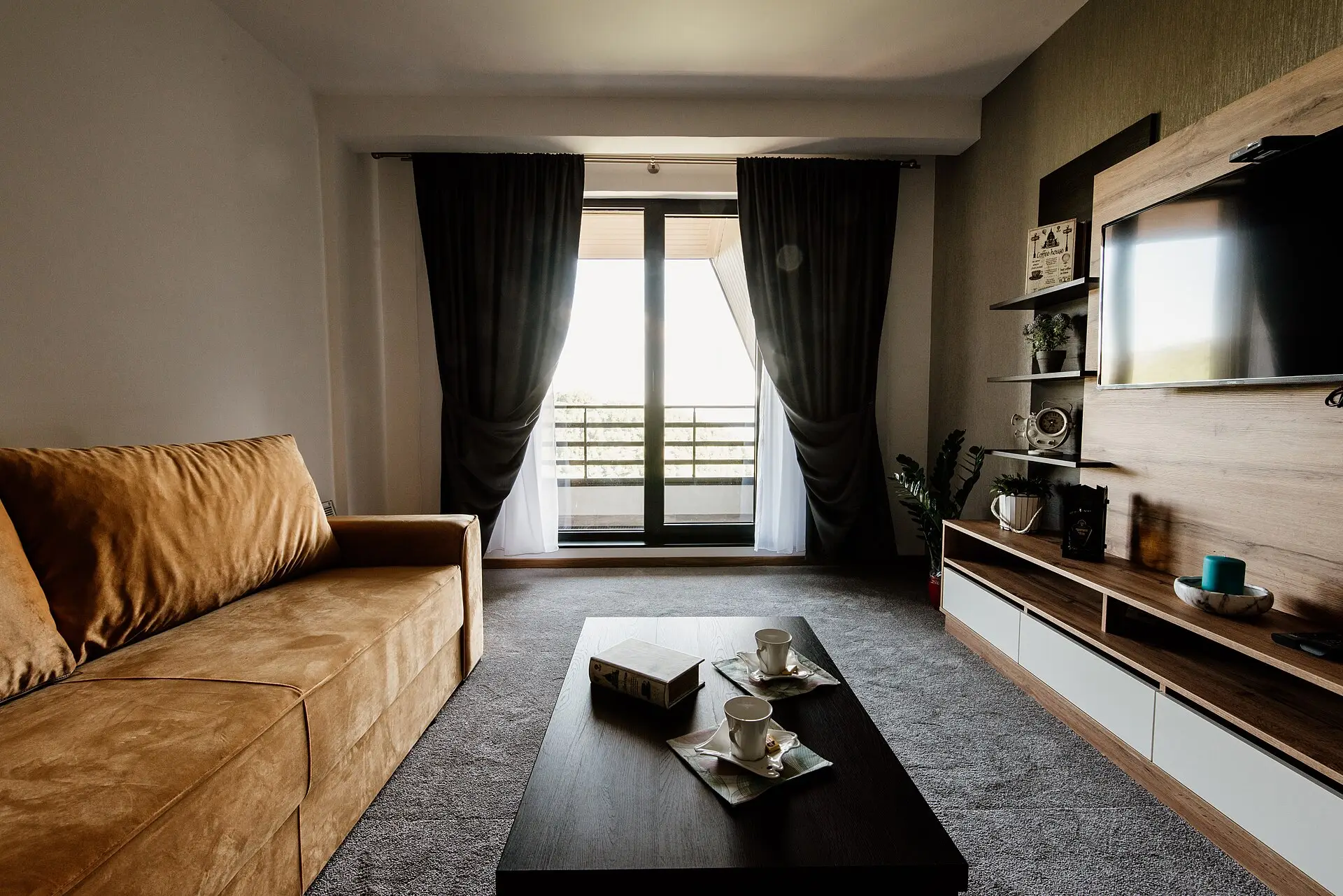 A warm living room with a tan leather sofa and floor-to-ceiling windows