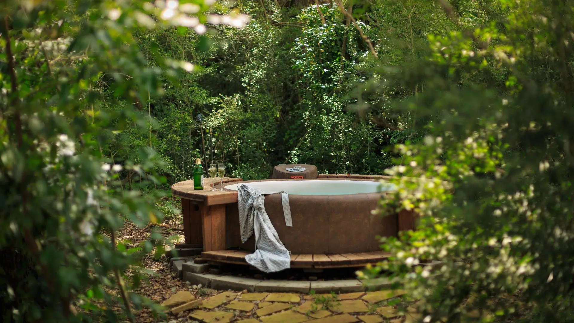 A round outdoor hot tub with a wooden surround in a leafy garden